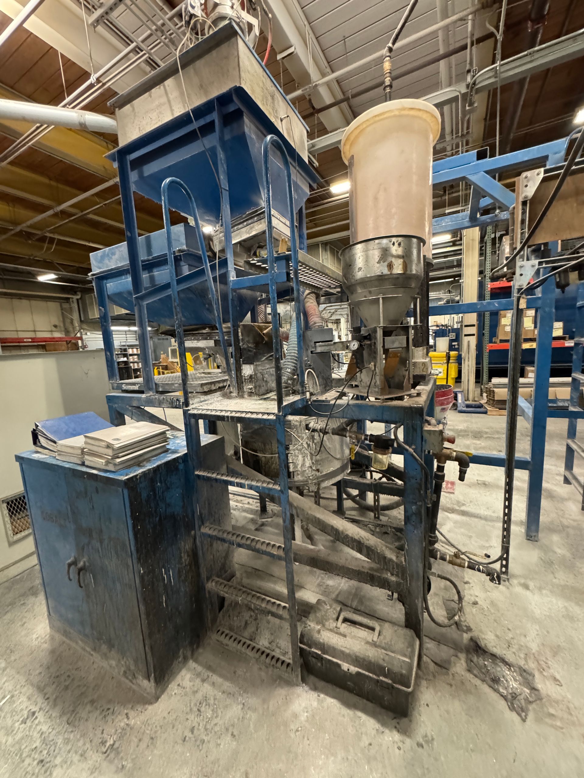 Industrial machinery, blue frame, with hopper and storage tank, inside a factory.