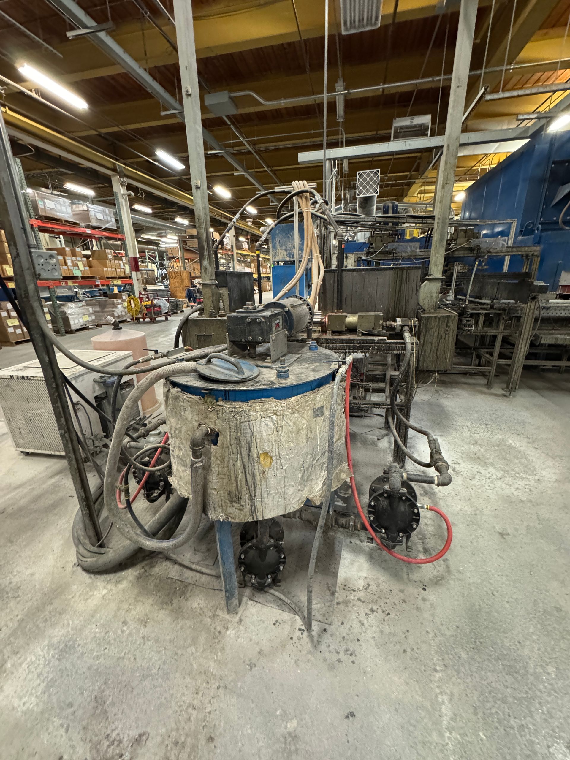 Industrial equipment in a warehouse setting, including a large mixing tank and connected machinery.