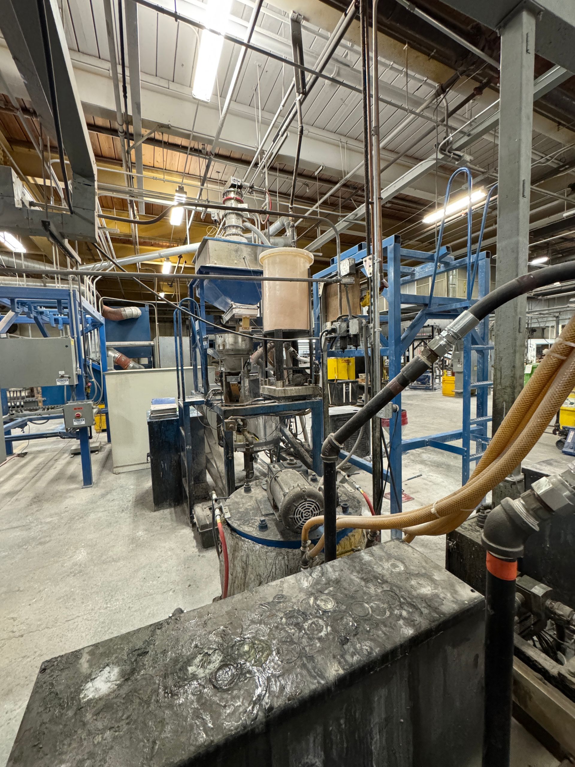 Industrial machinery in a factory setting, with pipes, tanks, and a gray concrete floor.