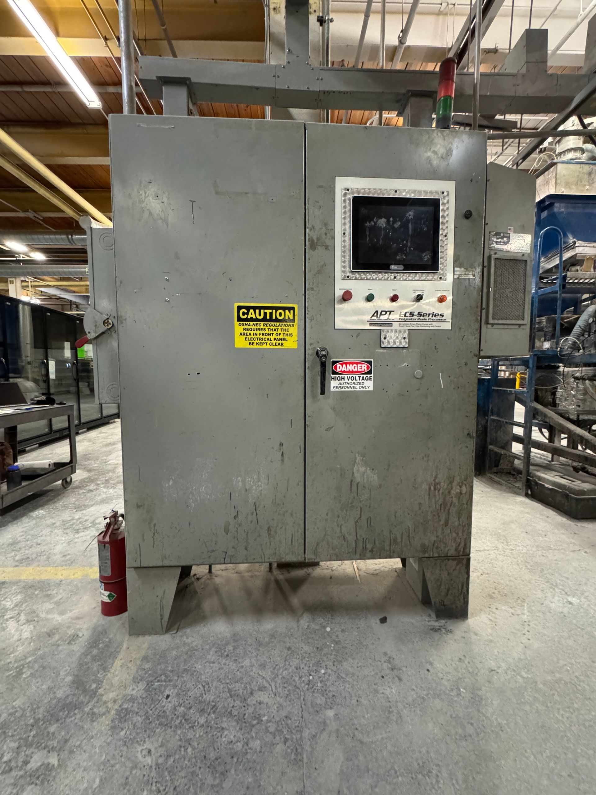 Grey industrial machine with a control panel and caution signs in a factory.