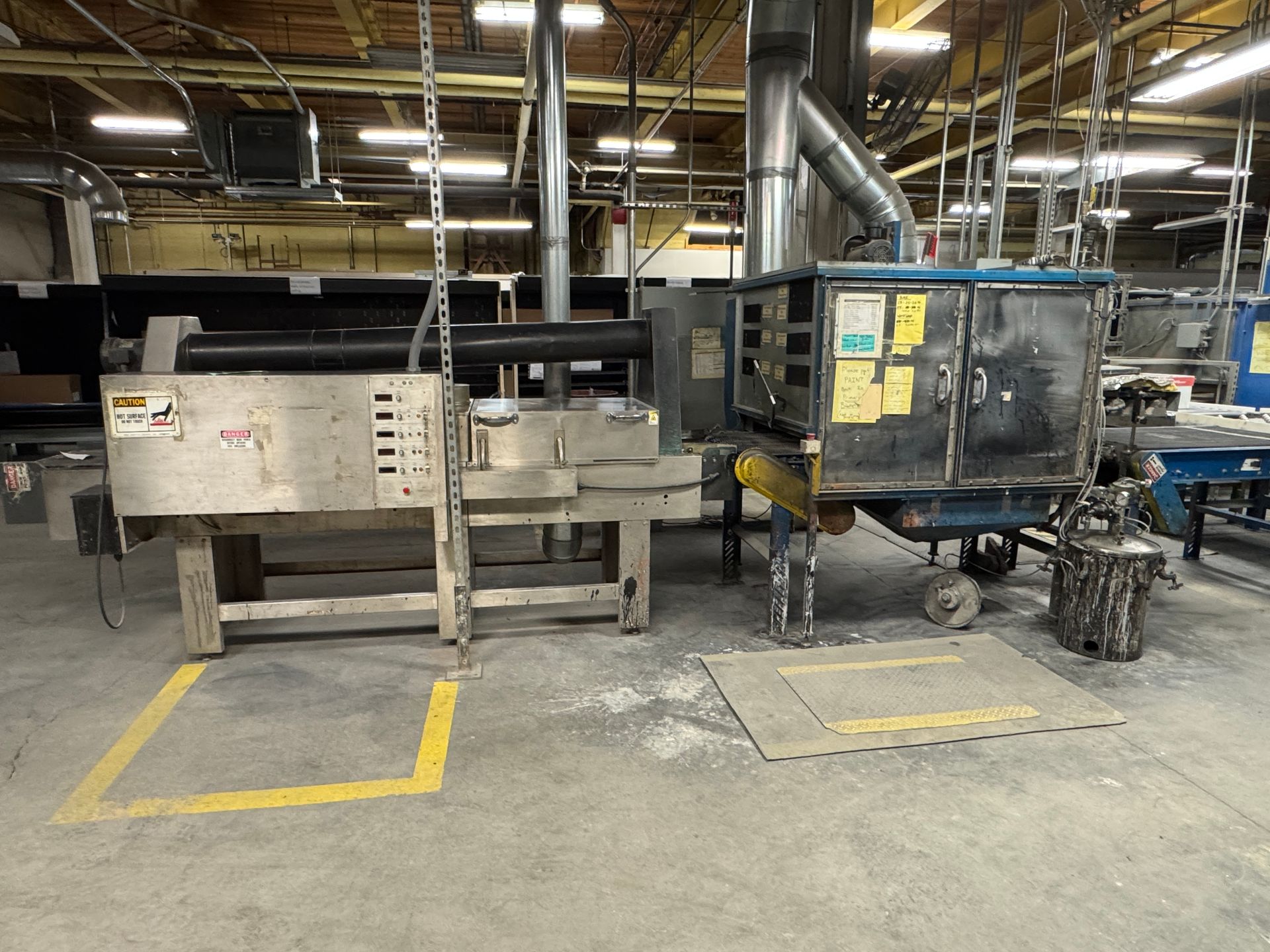 Industrial machinery in a factory setting, with a metallic rolling machine and an exhaust system.