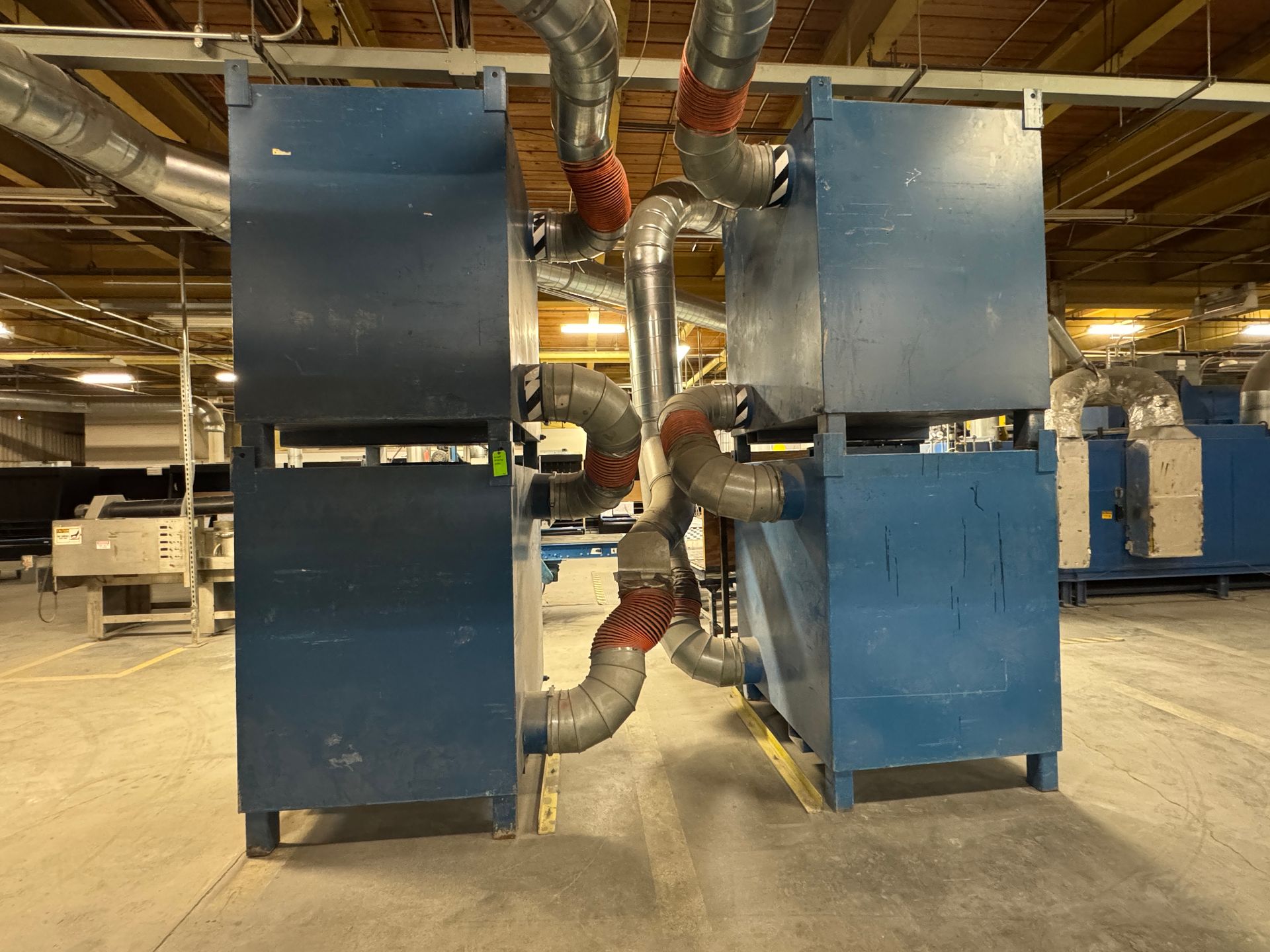 Two tall, blue industrial machines connected by ductwork and piping in a factory setting.