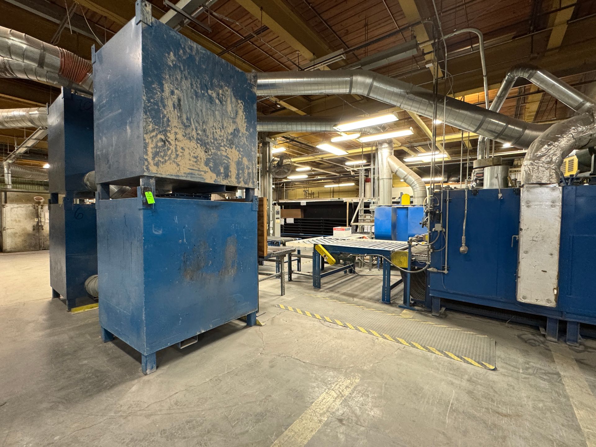 Blue industrial machinery in a factory setting. Conveyor belt and ventilation ducts are visible.