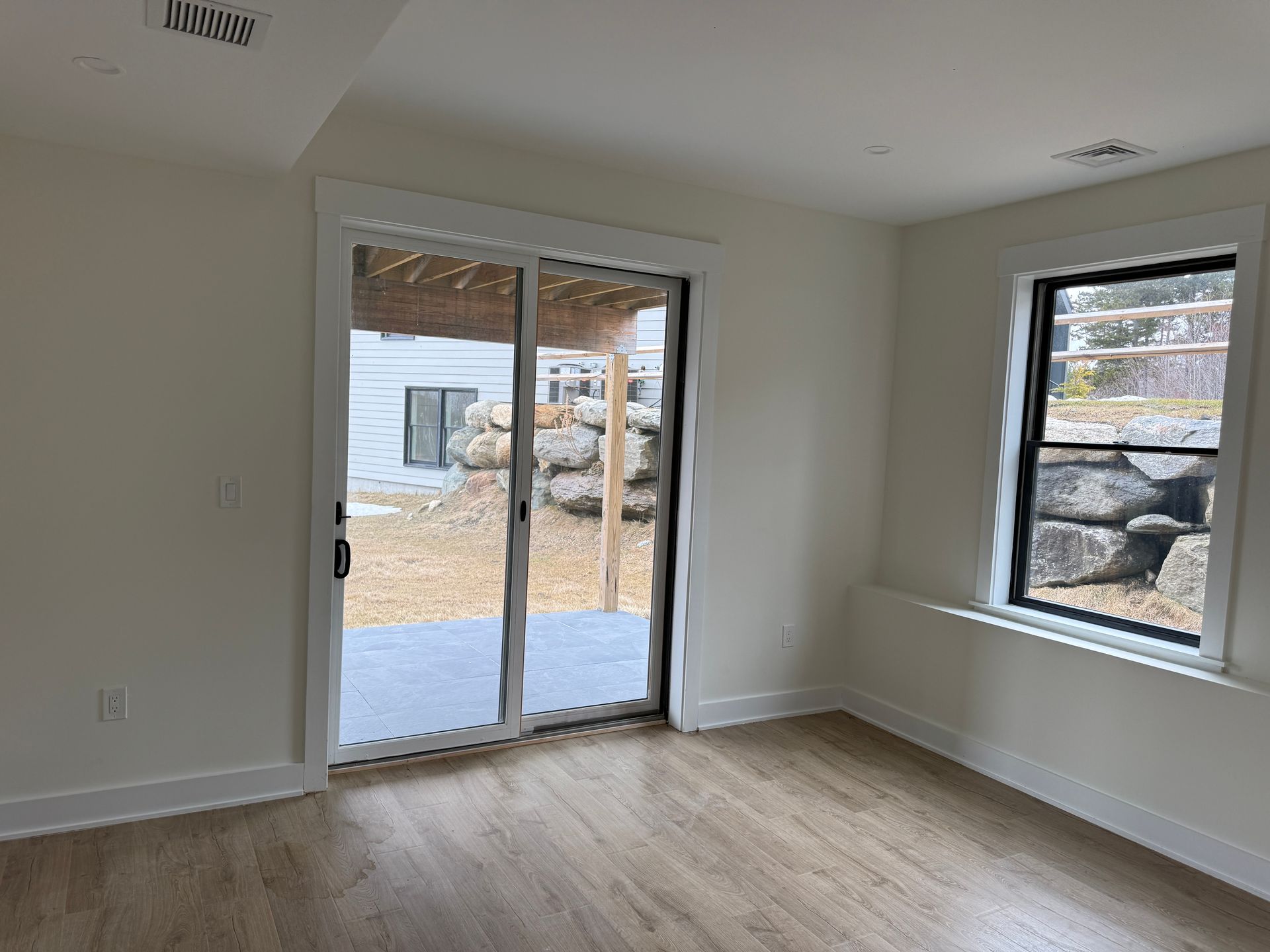 An empty room with light wood floors, white walls, a sliding glass door leading to a patio, and one window.