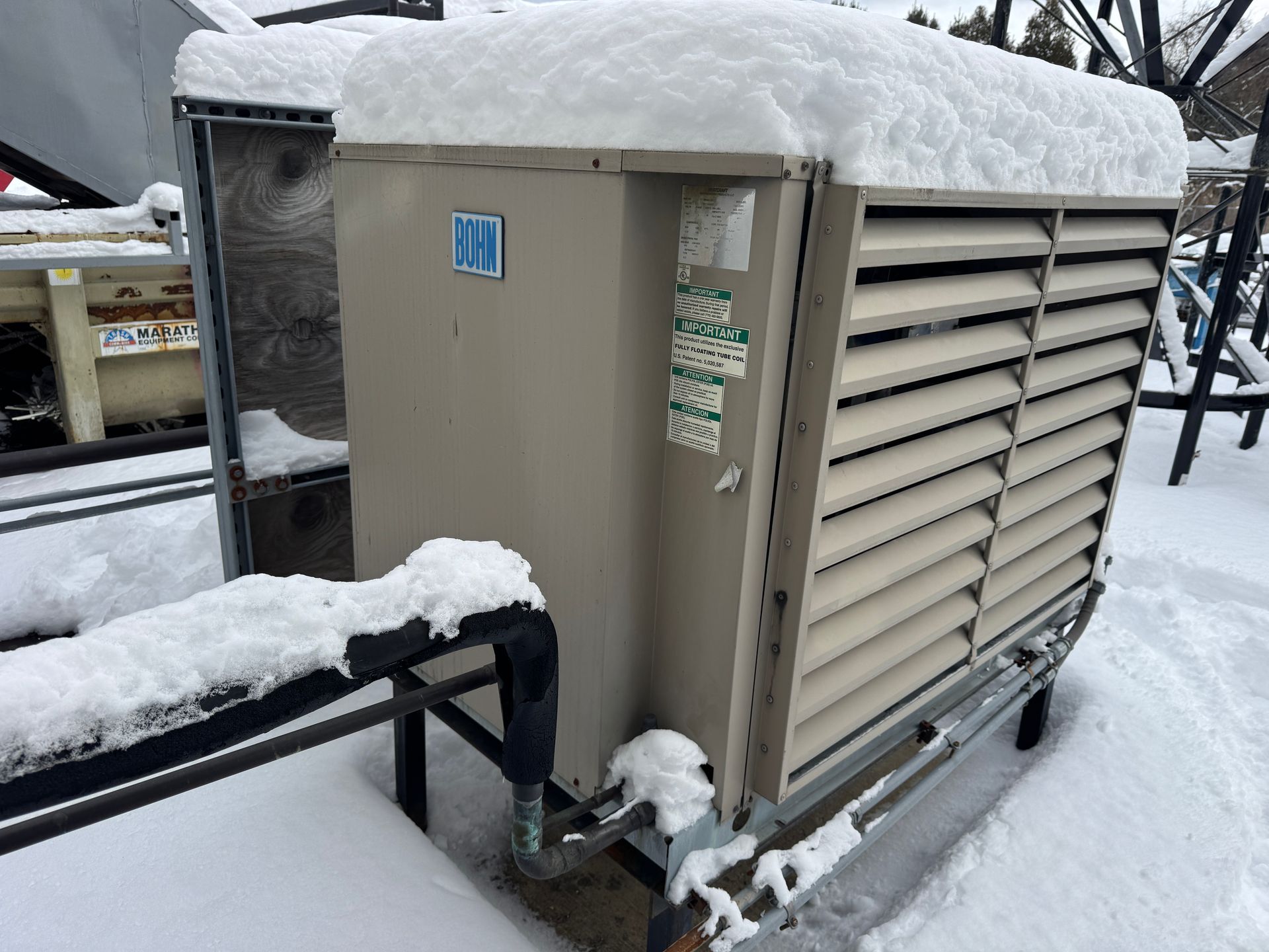 Snow-covered industrial cooling unit outdoors, beige with slatted side panels, metal frame, set in snow.