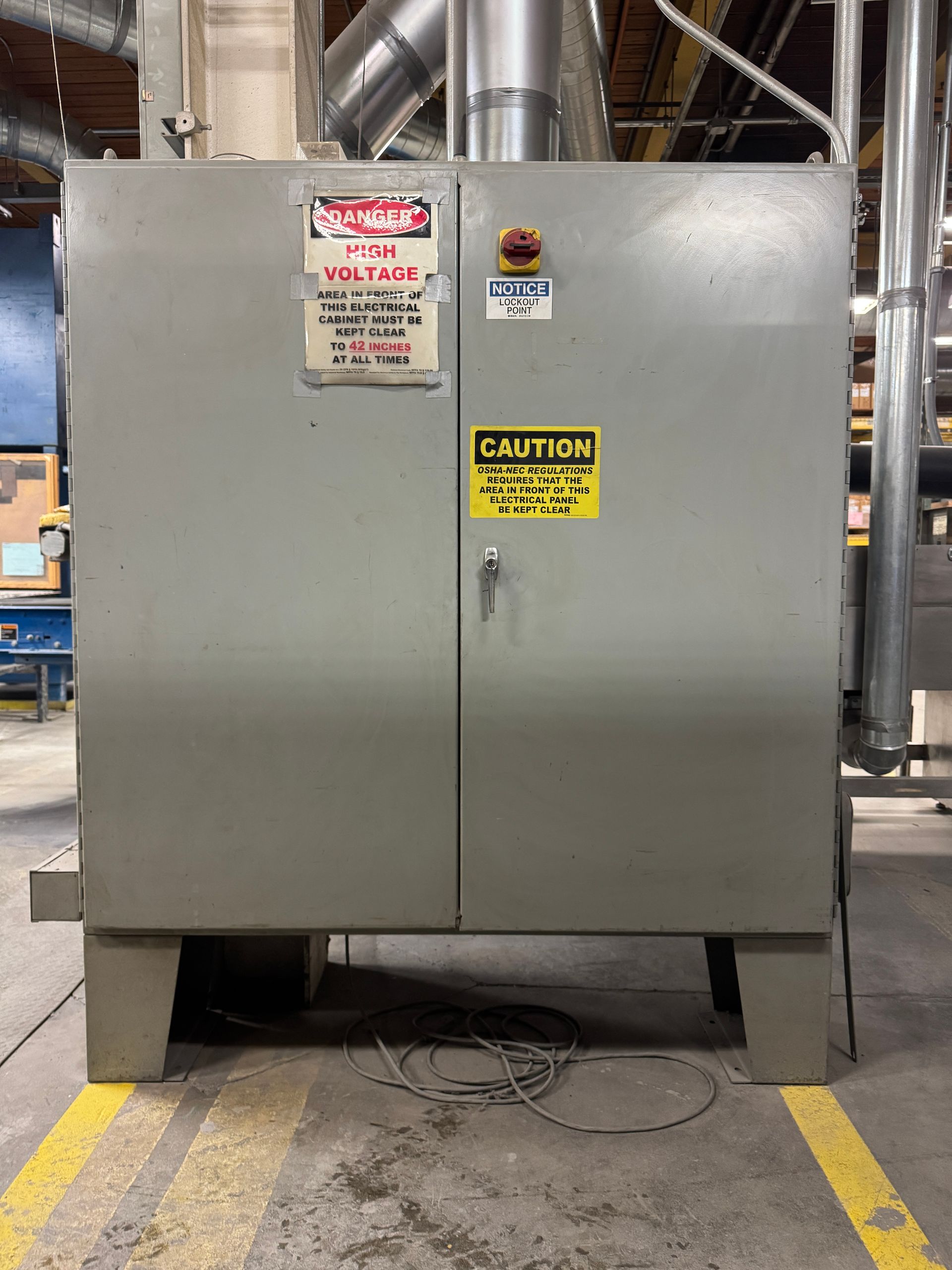 Gray electrical cabinet with warning signs on factory floor.