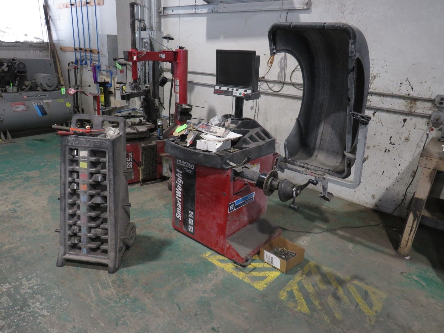 Tire balancing machine in a garage. Red and black machine with a computer screen and a protective cover.