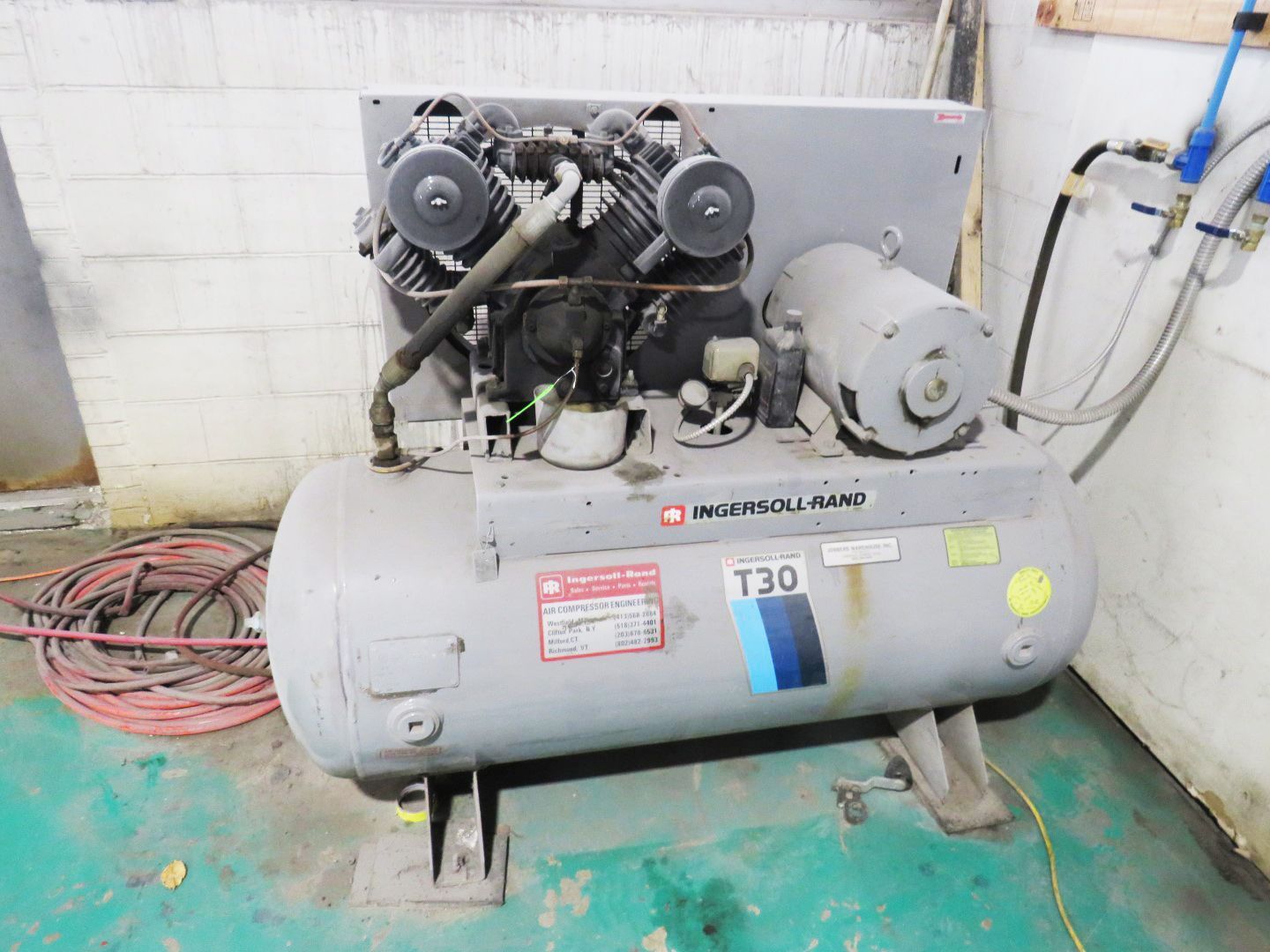 Gray industrial air compressor in a corner, with a horizontal tank and engine above.