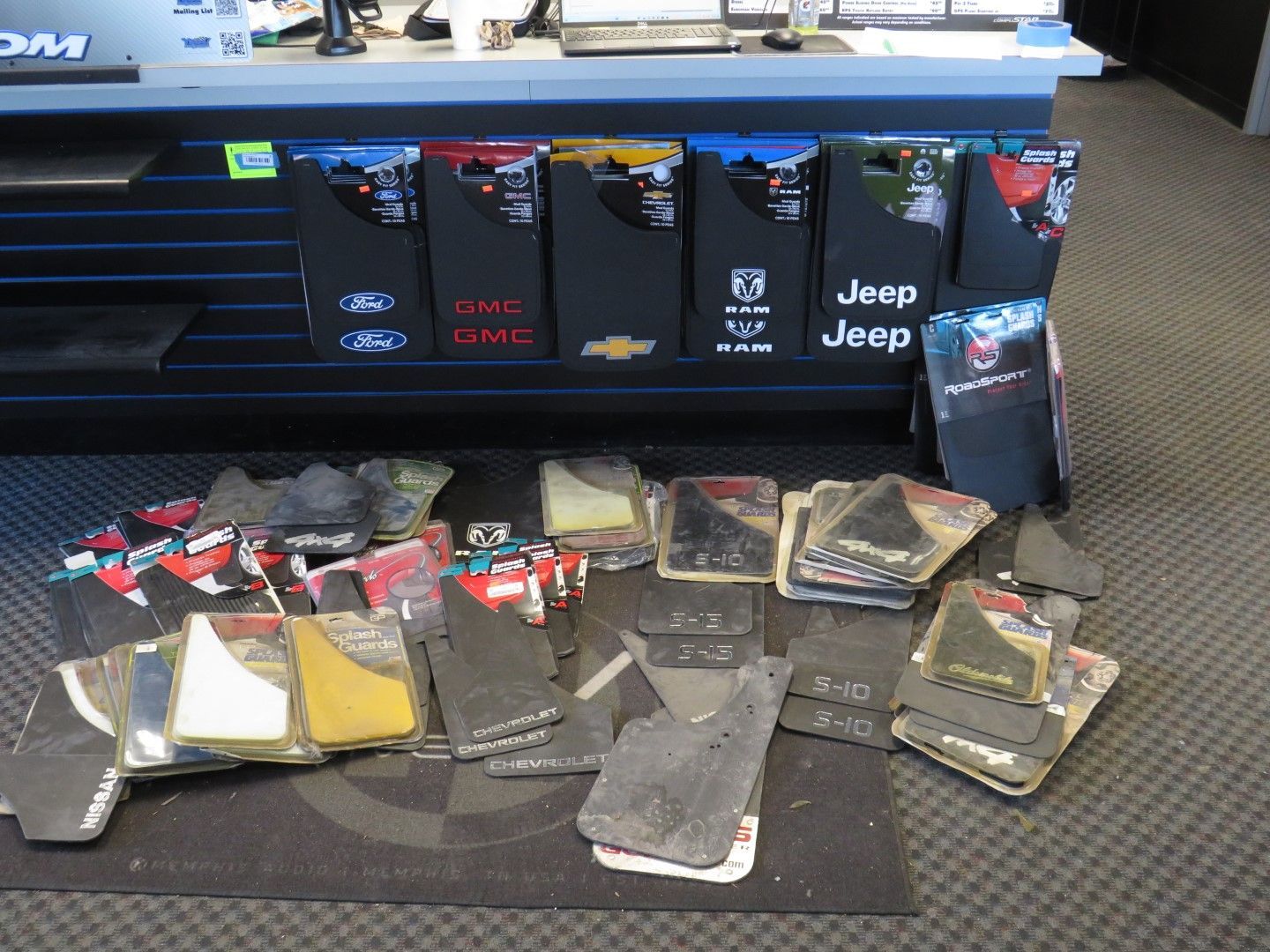 Car floor mats for sale displayed in a store, with branded display signs and logo.