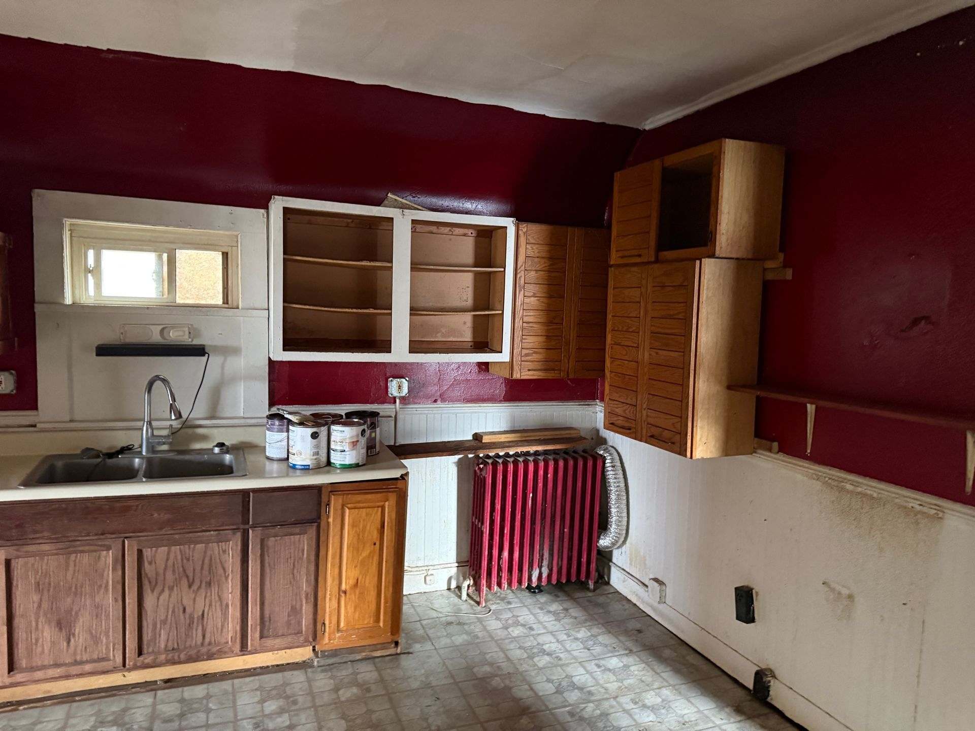 A kitchen with dark red walls, wood cabinets, a sink, and a red radiator against a white wall.