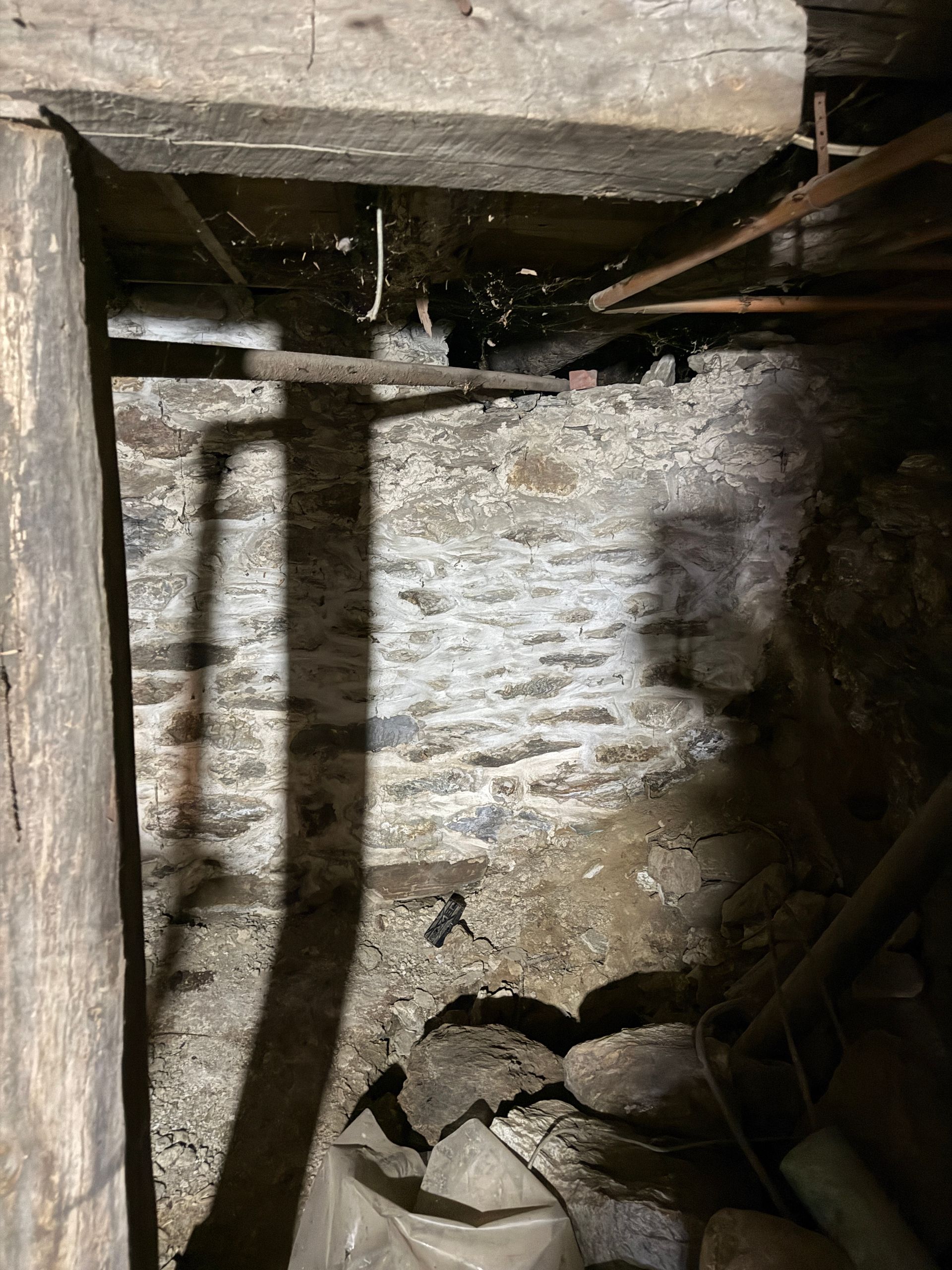 A basement corner featuring a rough stone wall, wooden structural beams.