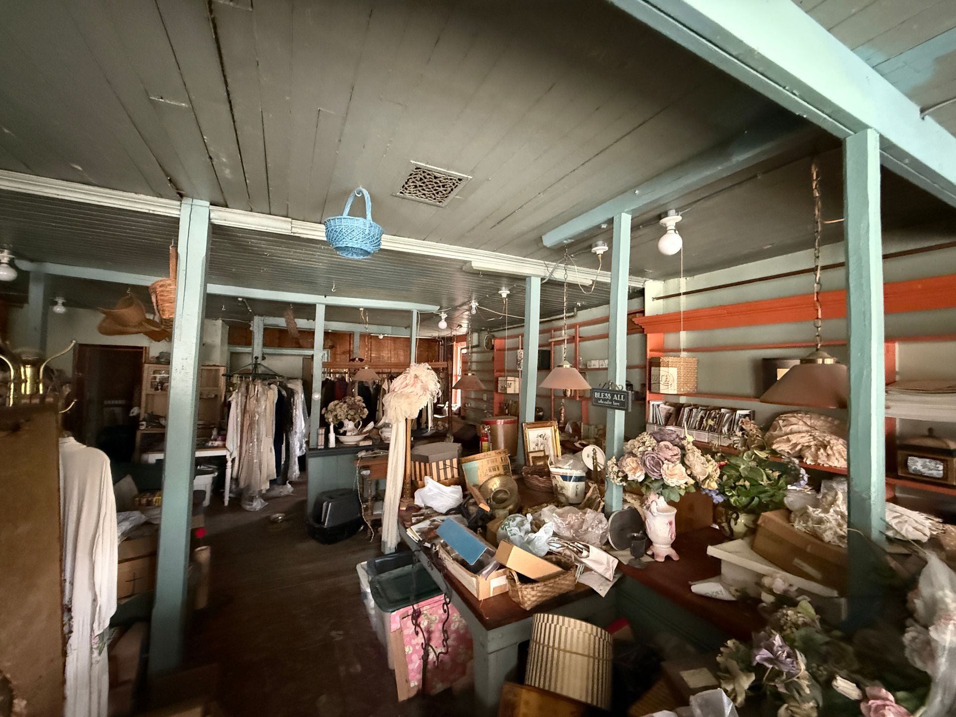 An interior of a vintage shop featuring clothing racks, floral arrangements, and various decorative items.