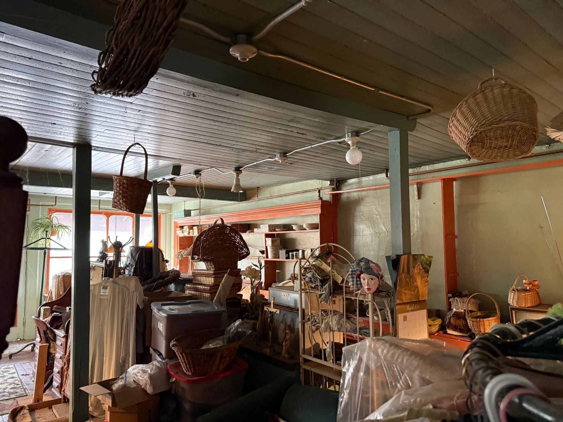 A shop interior filled with baskets, clothing, shelving, and various items under a wood-paneled ceiling.
