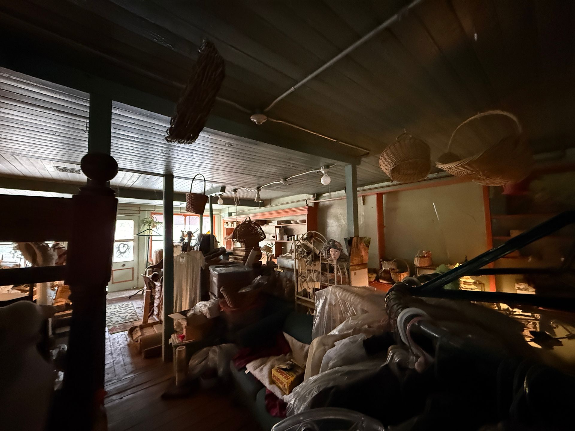 An interior shot of a room, featuring wicker baskets hanging from the ceiling, furniture, and personal items.