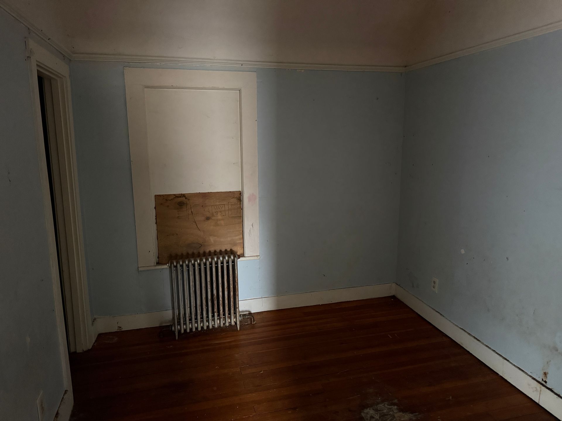 An empty room with blue walls, hardwood floors, a cast-iron radiator.