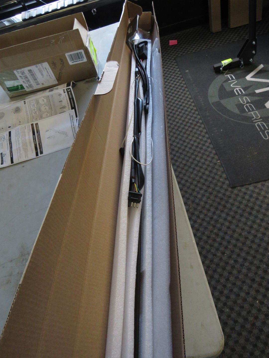 Long, narrow box open on a table, containing a long, black object wrapped in white foam.