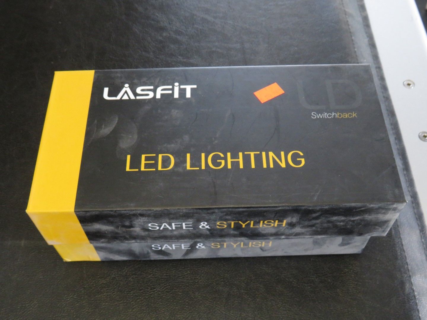 Black and yellow Lasfit LED Lighting box, dusty, on a dark surface.