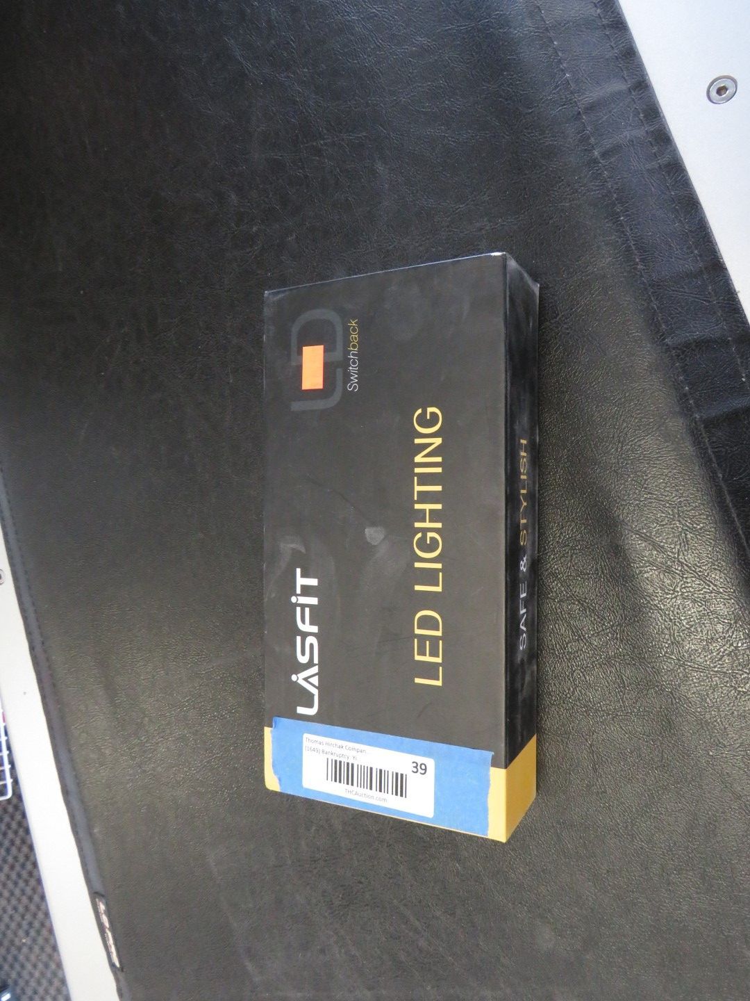 Black box of Lasfit LED Lighting with gold text and a blue label, on a black surface.