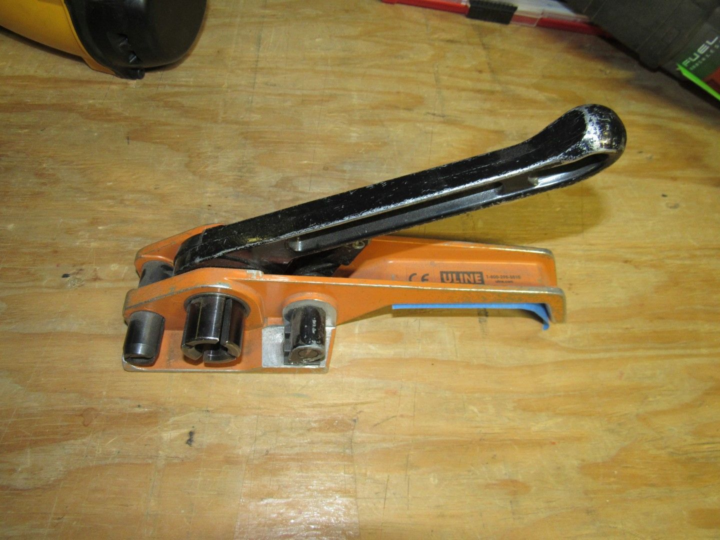 Orange and black strapping tool on a wooden surface.