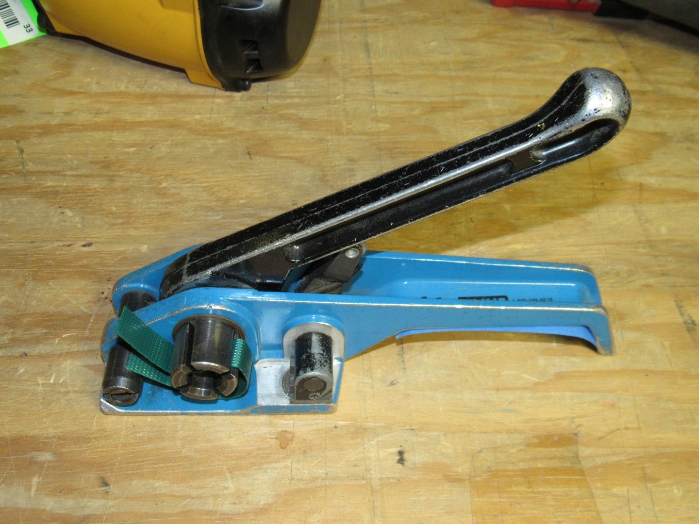 Blue plastic strapping tool with black handle, green strap, on a wood surface.