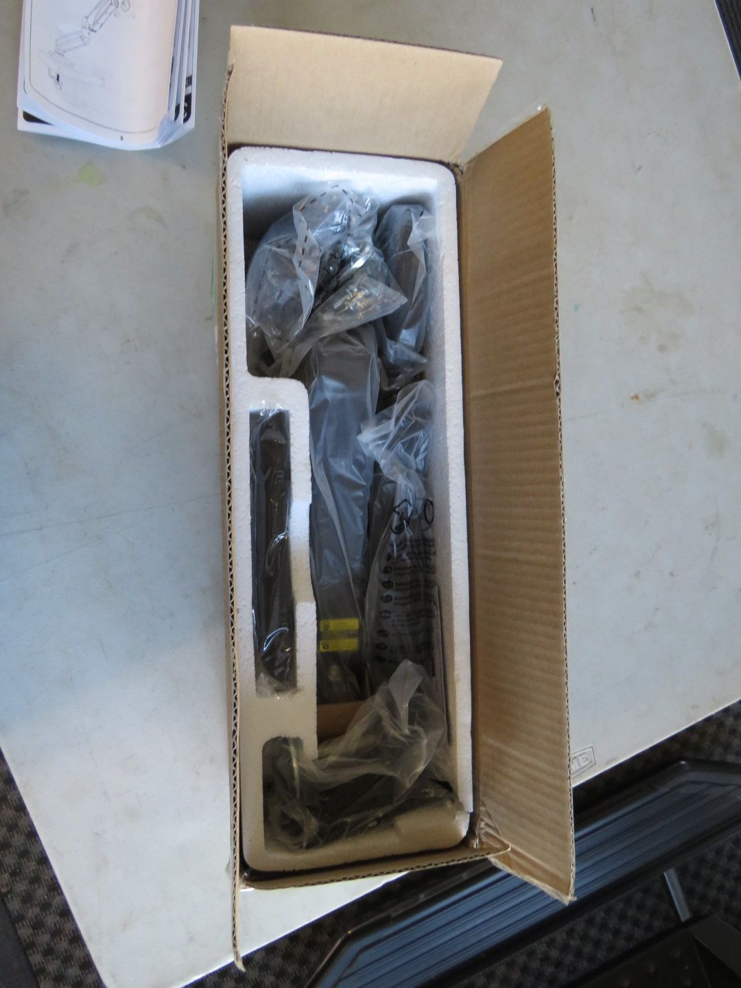 Open cardboard box with packaged black object, likely a vehicle accessory, cushioned with foam.