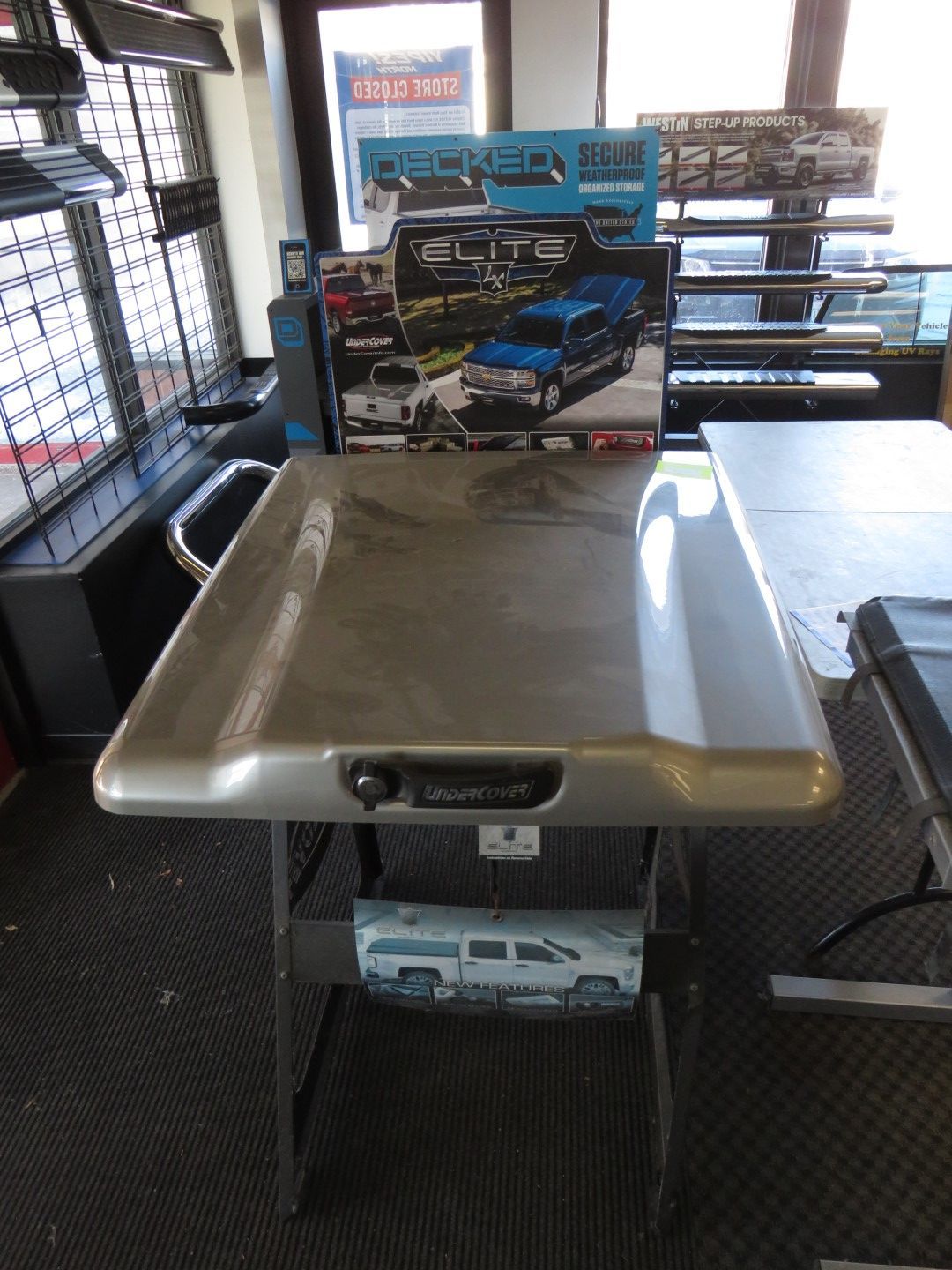 Silver truck bed cover on display in a store, with a handle and lock.