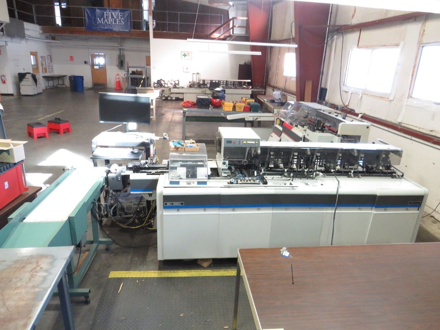 Factory with industrial equipment, including a collator and conveyor belt, likely for document processing.