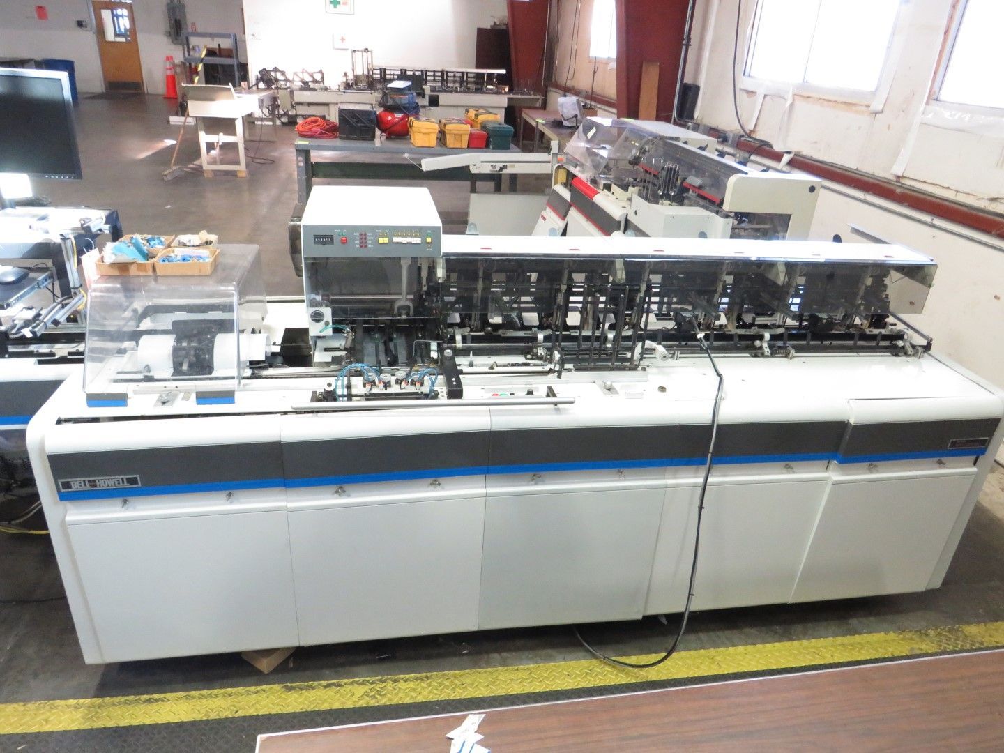 Large, industrial white and blue mailing machine in a factory setting.