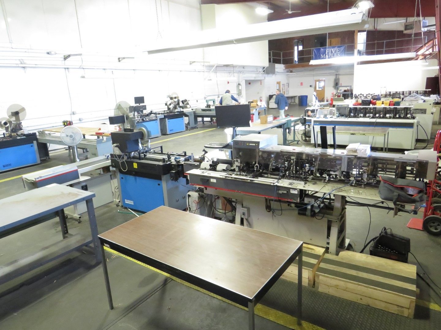 Manufacturing floor with machinery and tables. Blue and white equipment, bright interior.