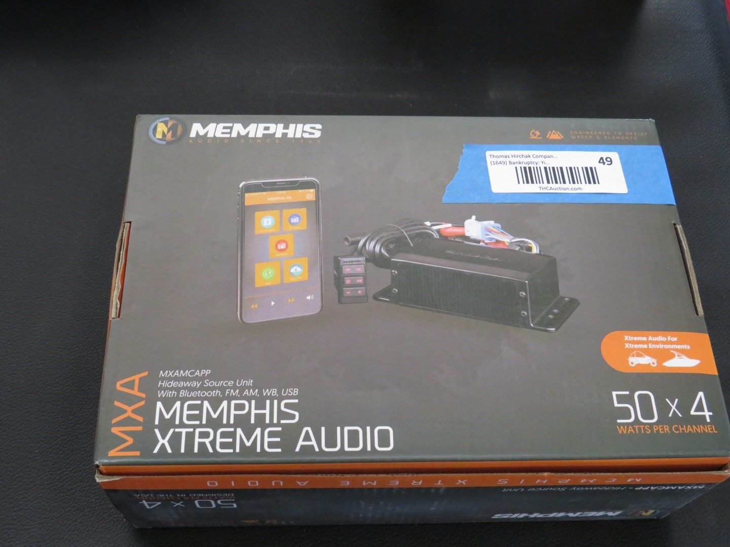 Box of Memphis Xtreme Audio amplifier with a remote control, against a dark background.