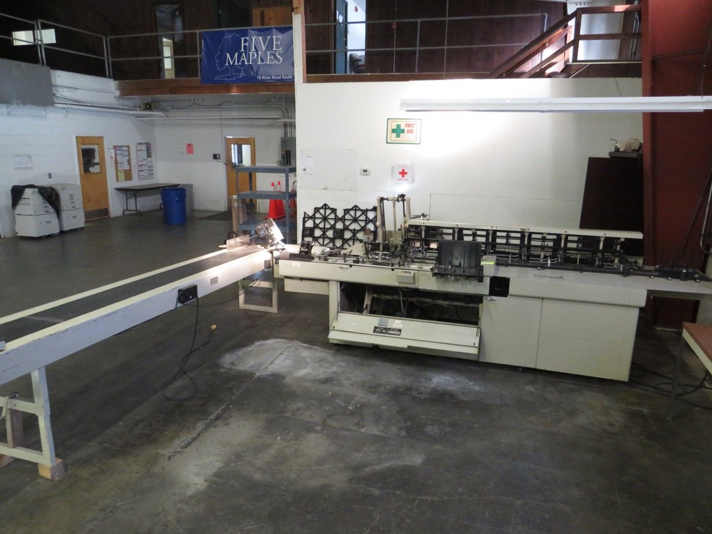 Industrial machine with conveyor belt in a warehouse setting; beige, gray, white, and black colors are present.