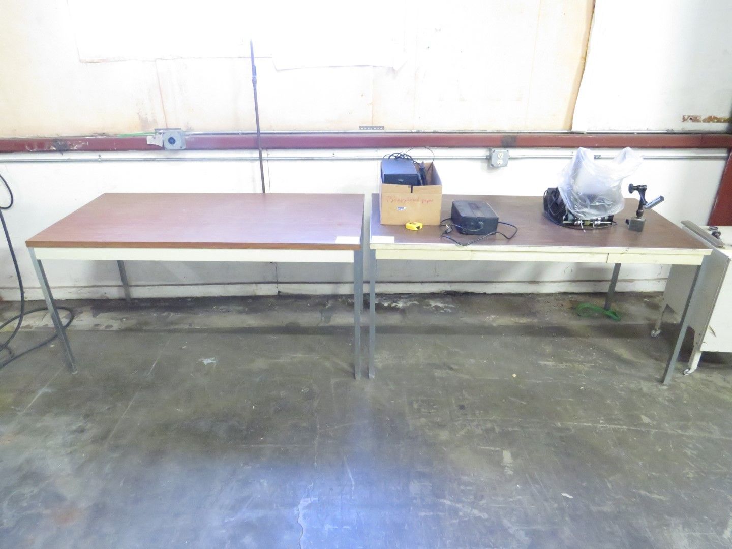 Two rectangular work tables in a room with tools and a concrete floor.
