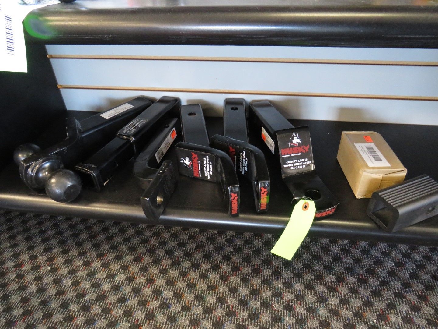 Black trailer hitches and accessories on a shelf in a store setting.