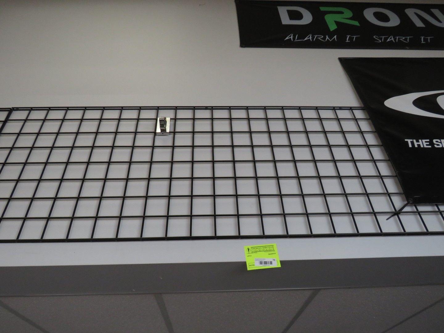 Black wire grid display on white wall with green and black signs above.