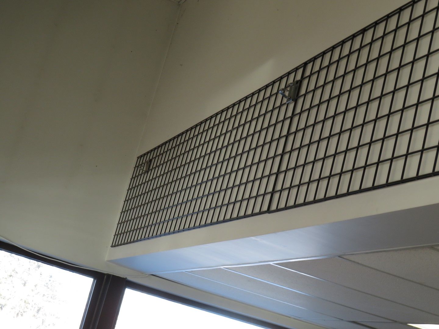 Black metal grid on a white ceiling, above a window, interior shot.
