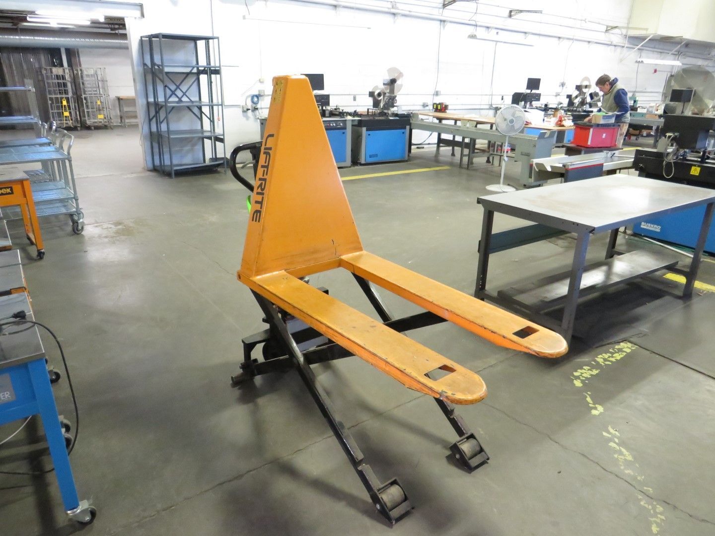 Orange pallet jack in a workshop with other equipment.