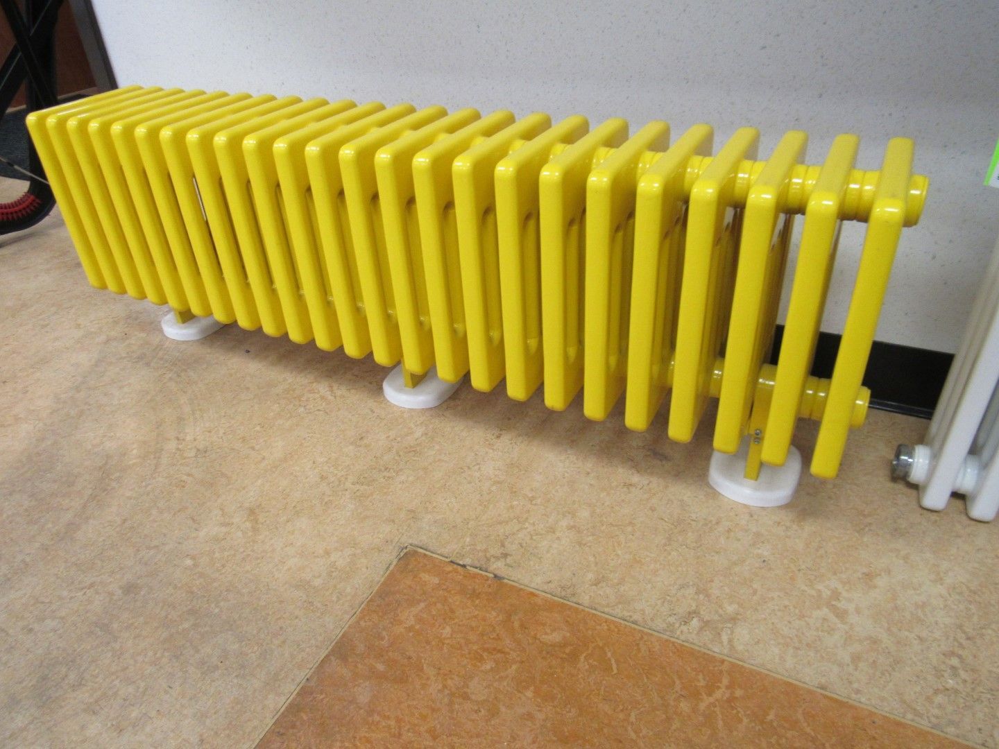 Yellow radiator on white feet in room with brown and tan floors.