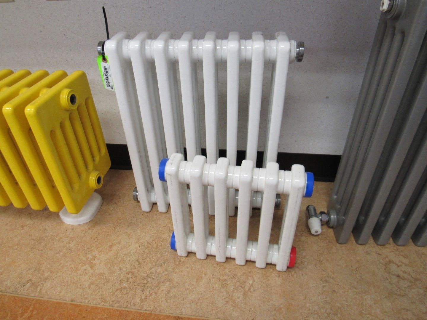 Radiators in various colors: yellow, white, and gray, displayed on a brown floor.