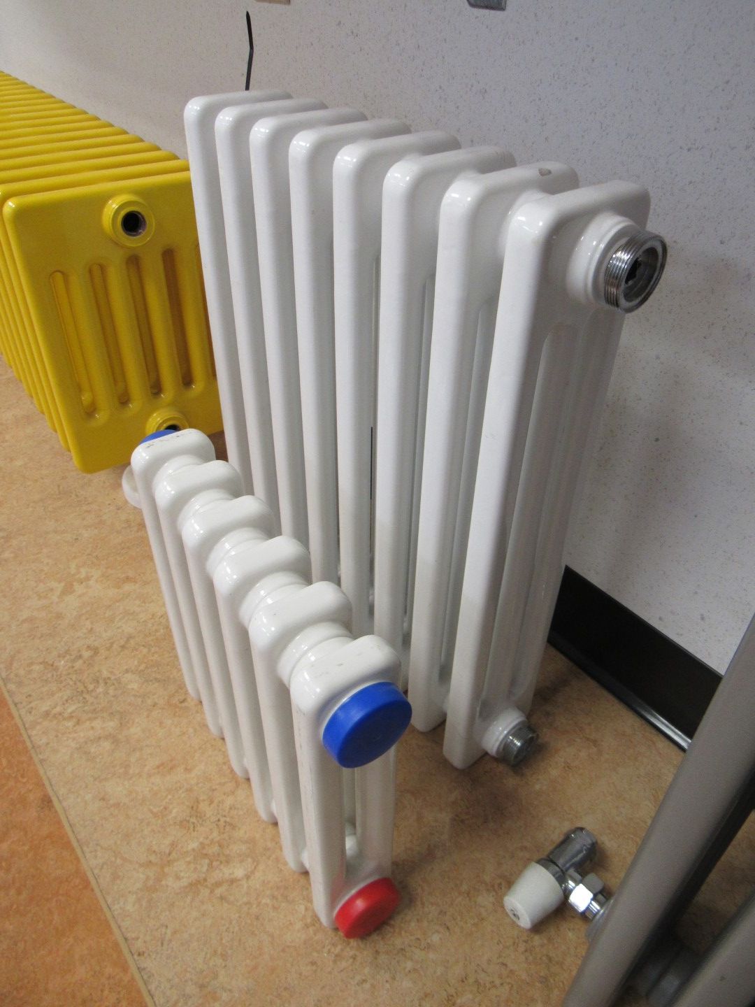 Three white and yellow radiators of different sizes in a room, with a valve on the floor.