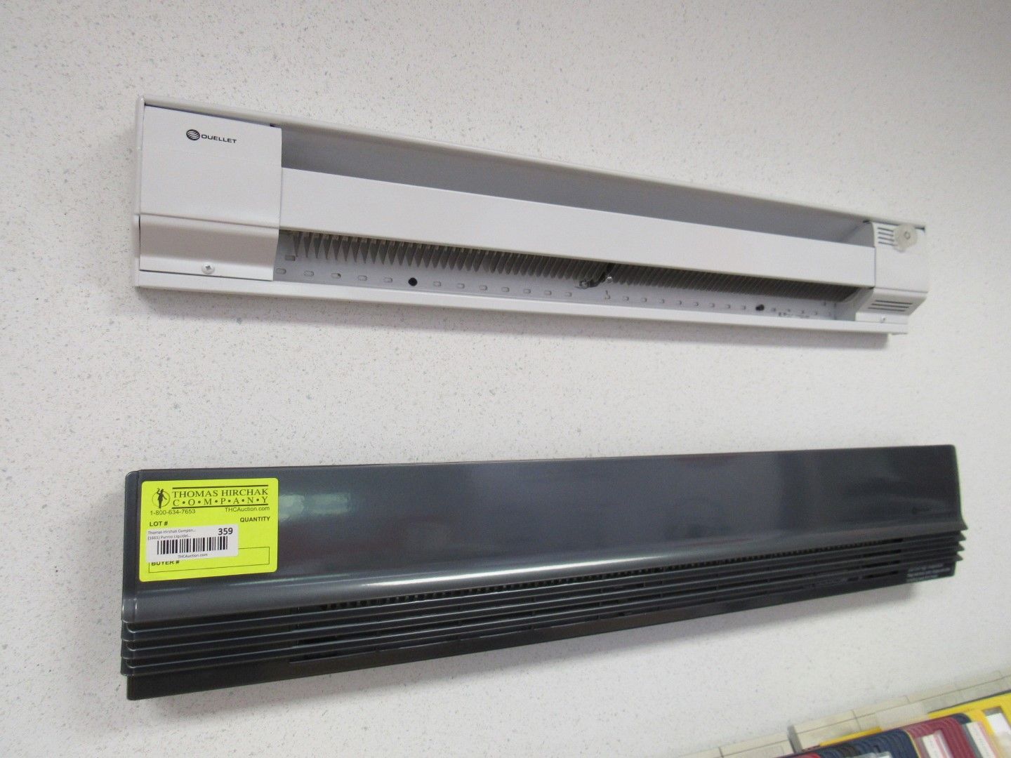Two baseboard heaters mounted on a white wall. The top one is white, and the bottom one is gray.