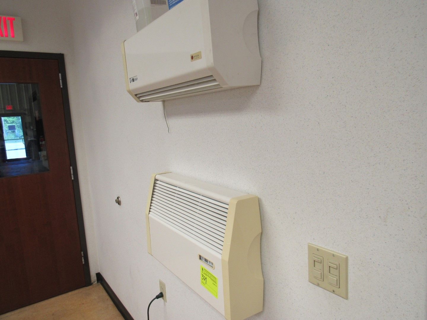 Two white HVAC units mounted on a white textured wall, next to a door.