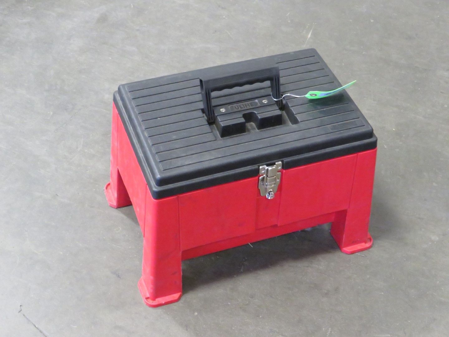 Red and black plastic toolbox with built-in step, handle, and clasp on a gray surface.