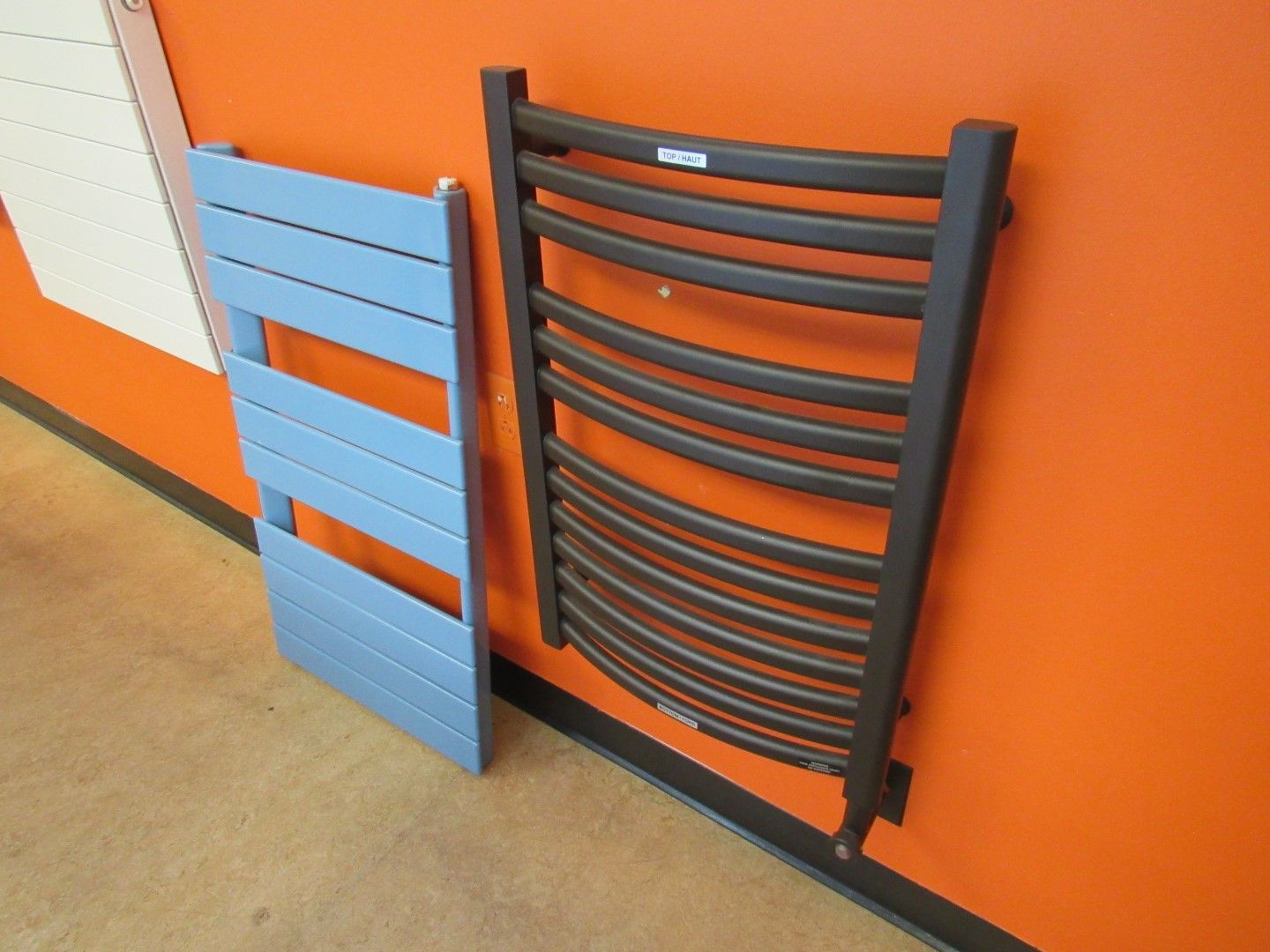 Two towel warmers, one blue and one dark brown, leaning against an orange wall.