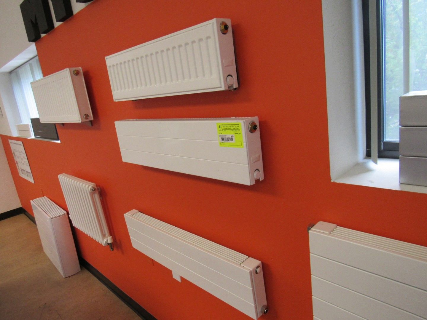 Wall display of white radiators against a red wall, showcasing various designs and sizes.