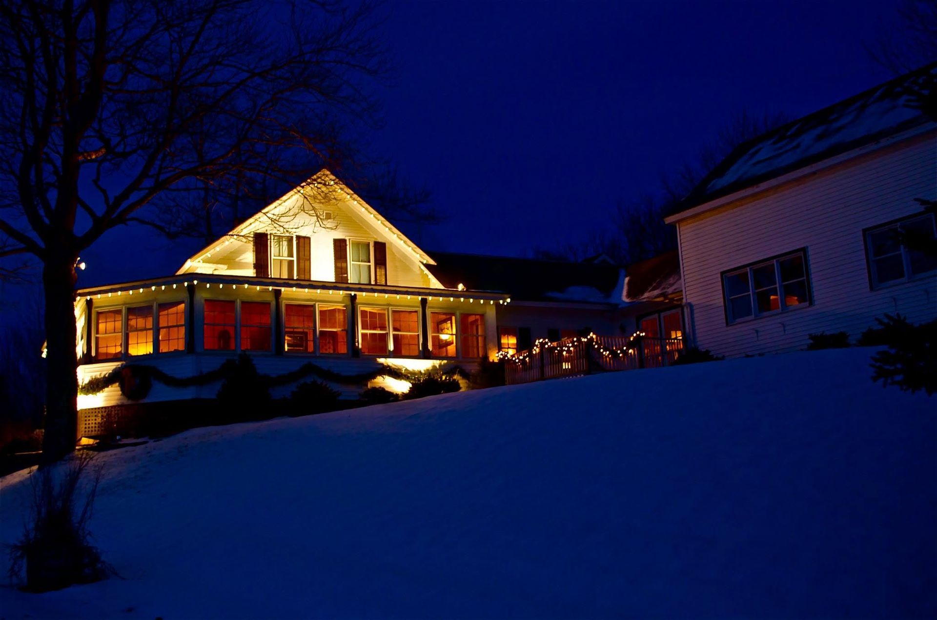 Snowy house glowing warmly at night under a deep blue sky