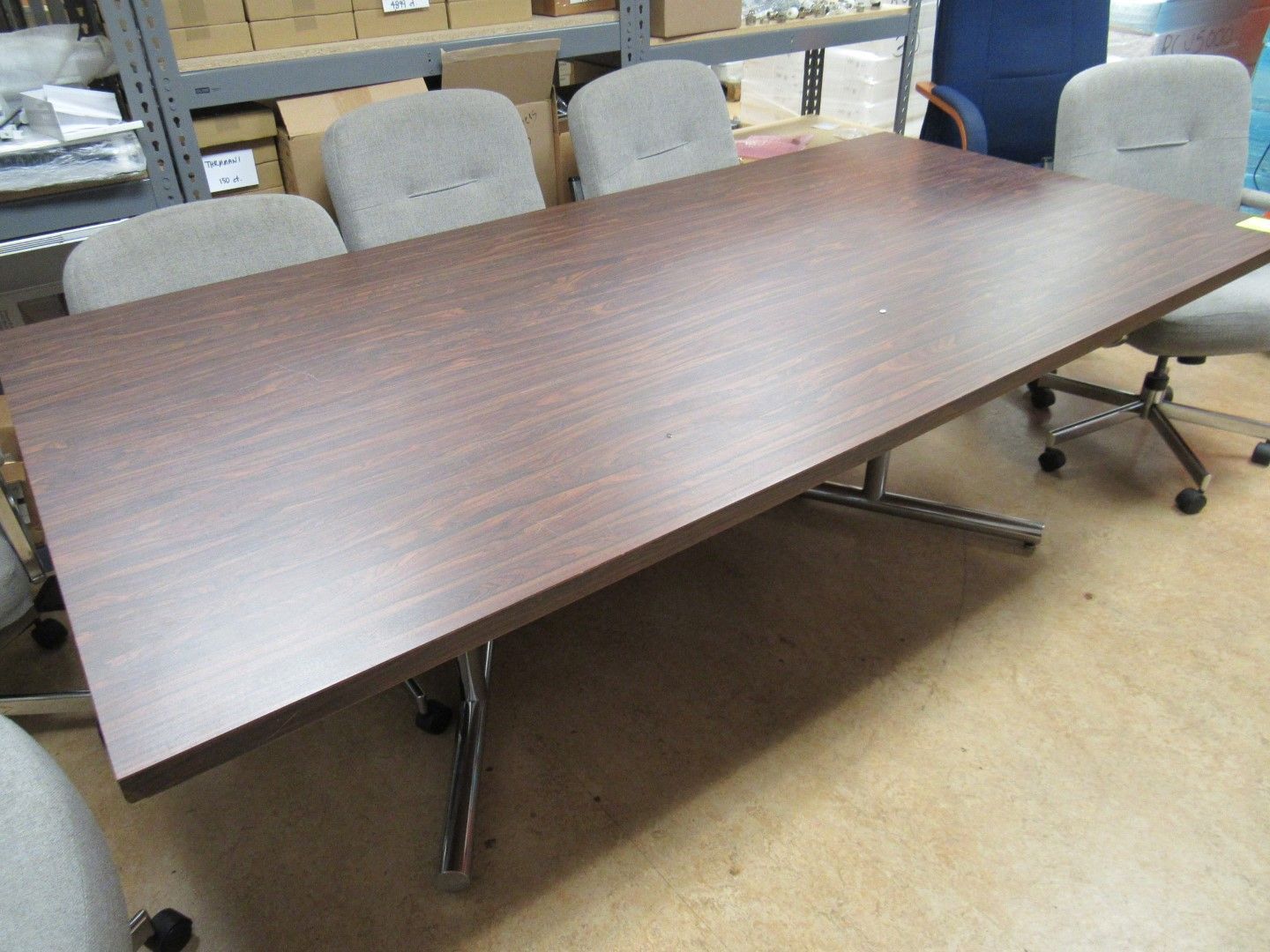 Conference table with brown tabletop, surrounded by gray chairs in a room.