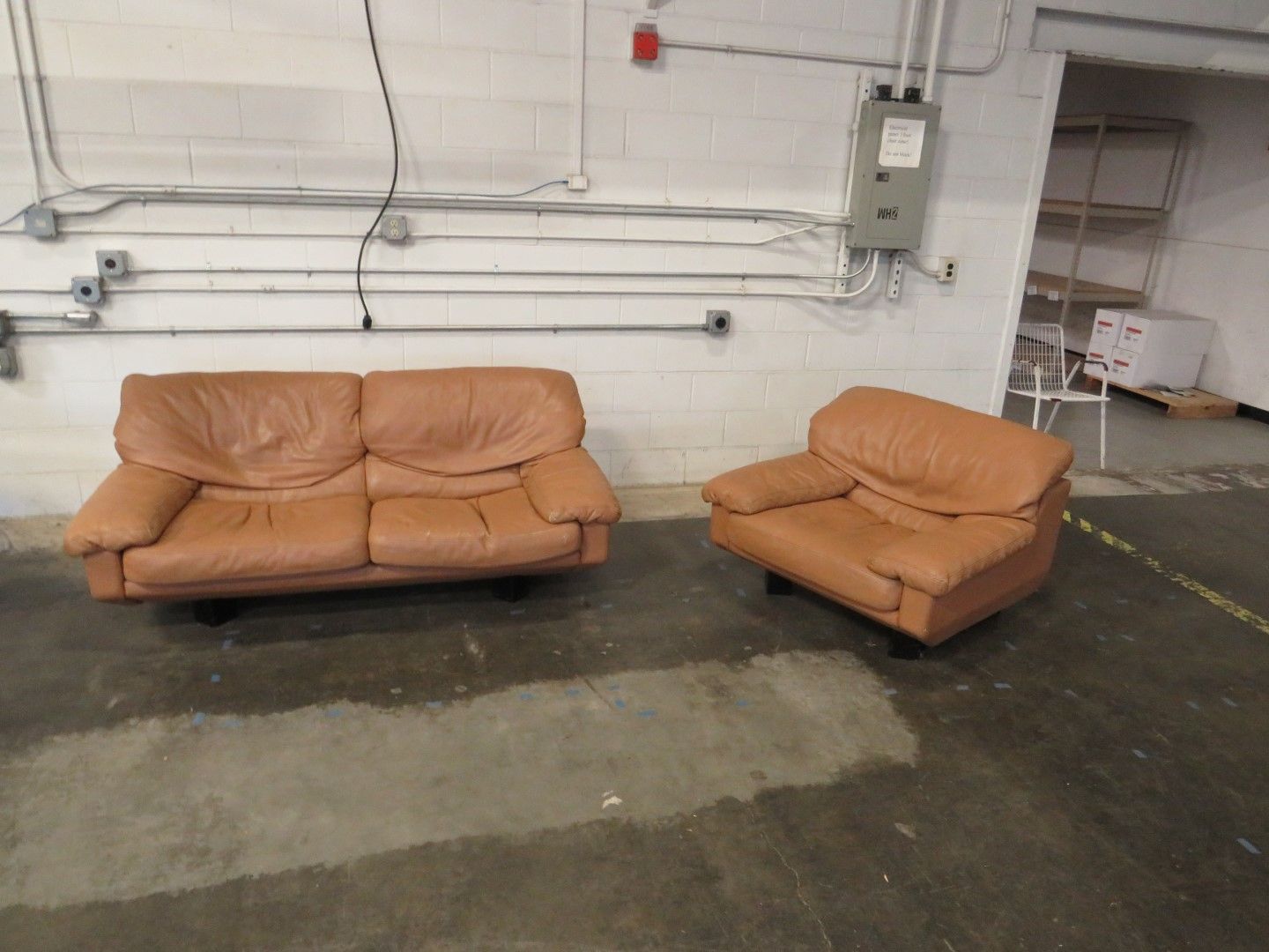 Tan leather sofa and armchair in a warehouse setting.