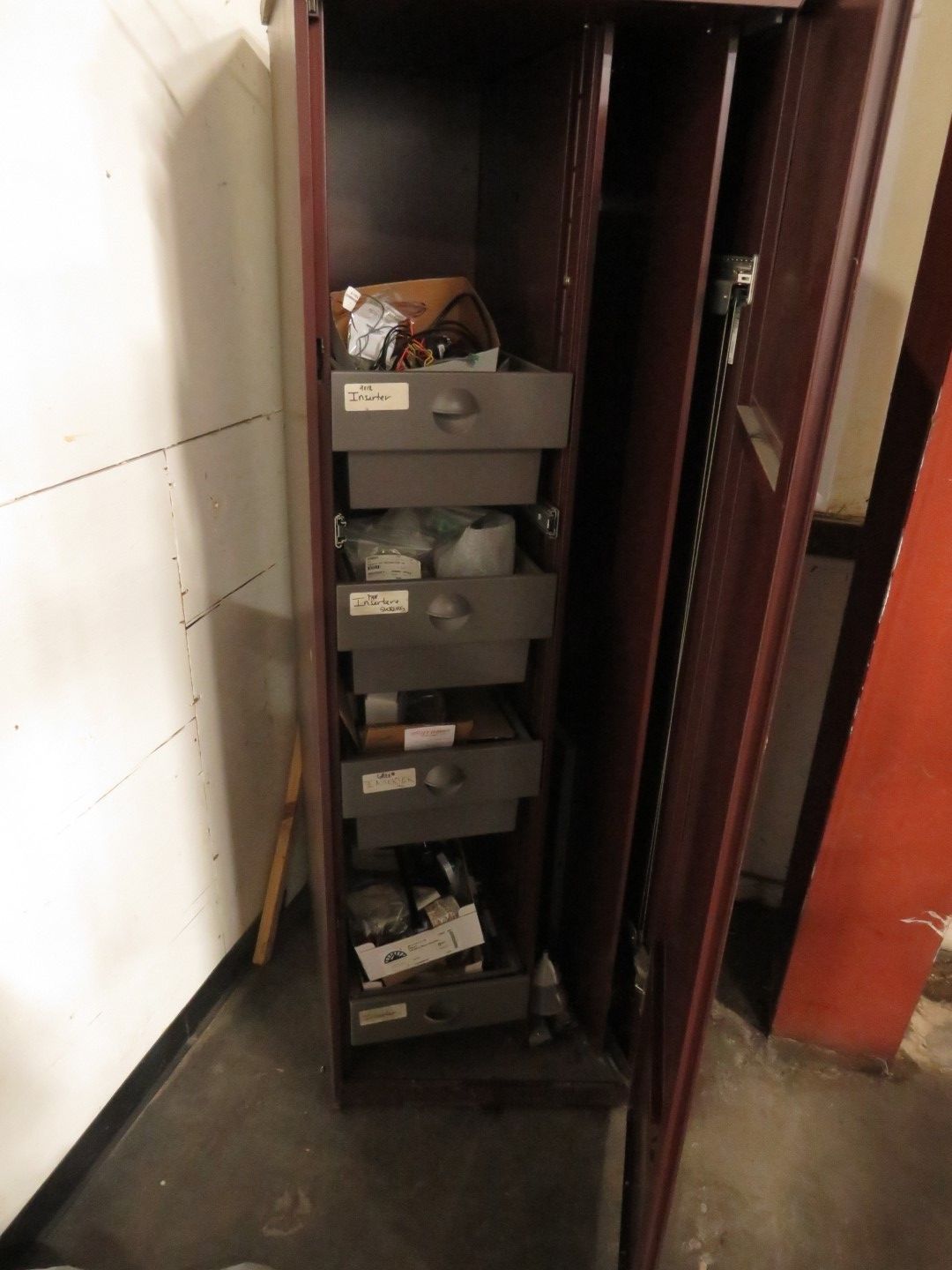A tall, open cabinet with multiple drawers; contents include various items.