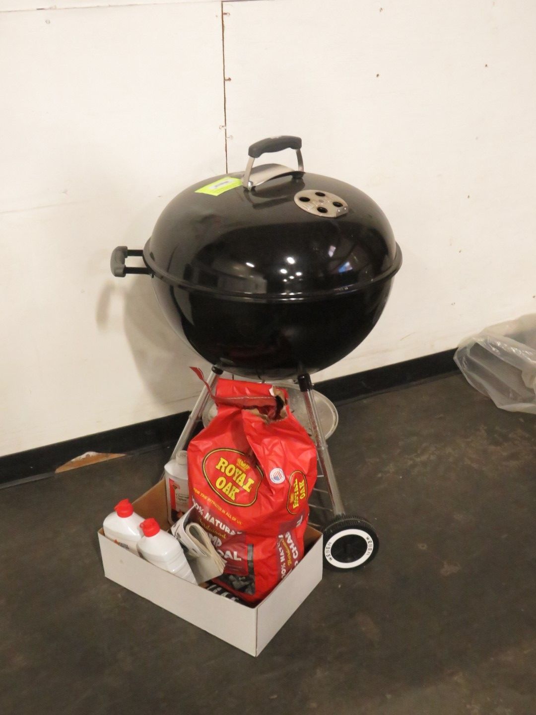 Black charcoal grill with a bag of charcoal and other supplies in a box.