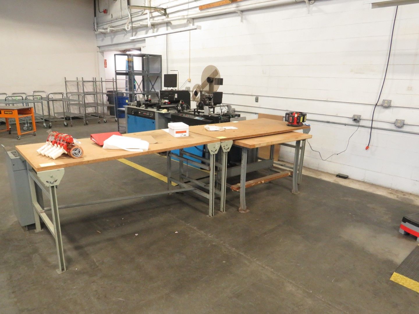 A workshop with multiple work tables, tools, and a machine set up on a concrete floor.